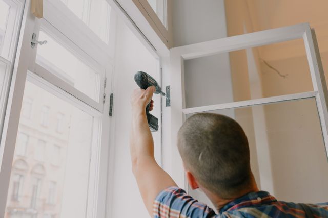 a person fixing a window hinge with a drill