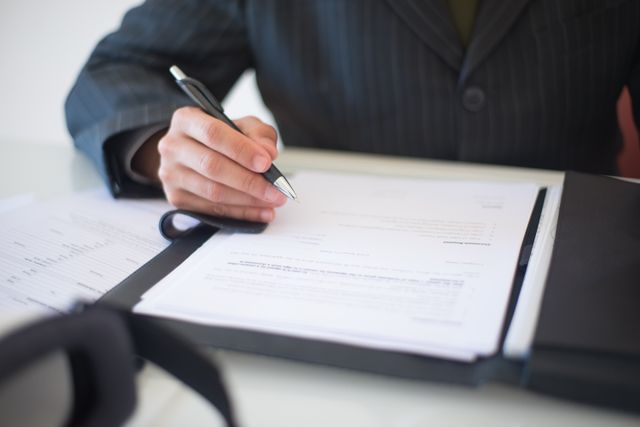 person in a suit signing documents with a pen