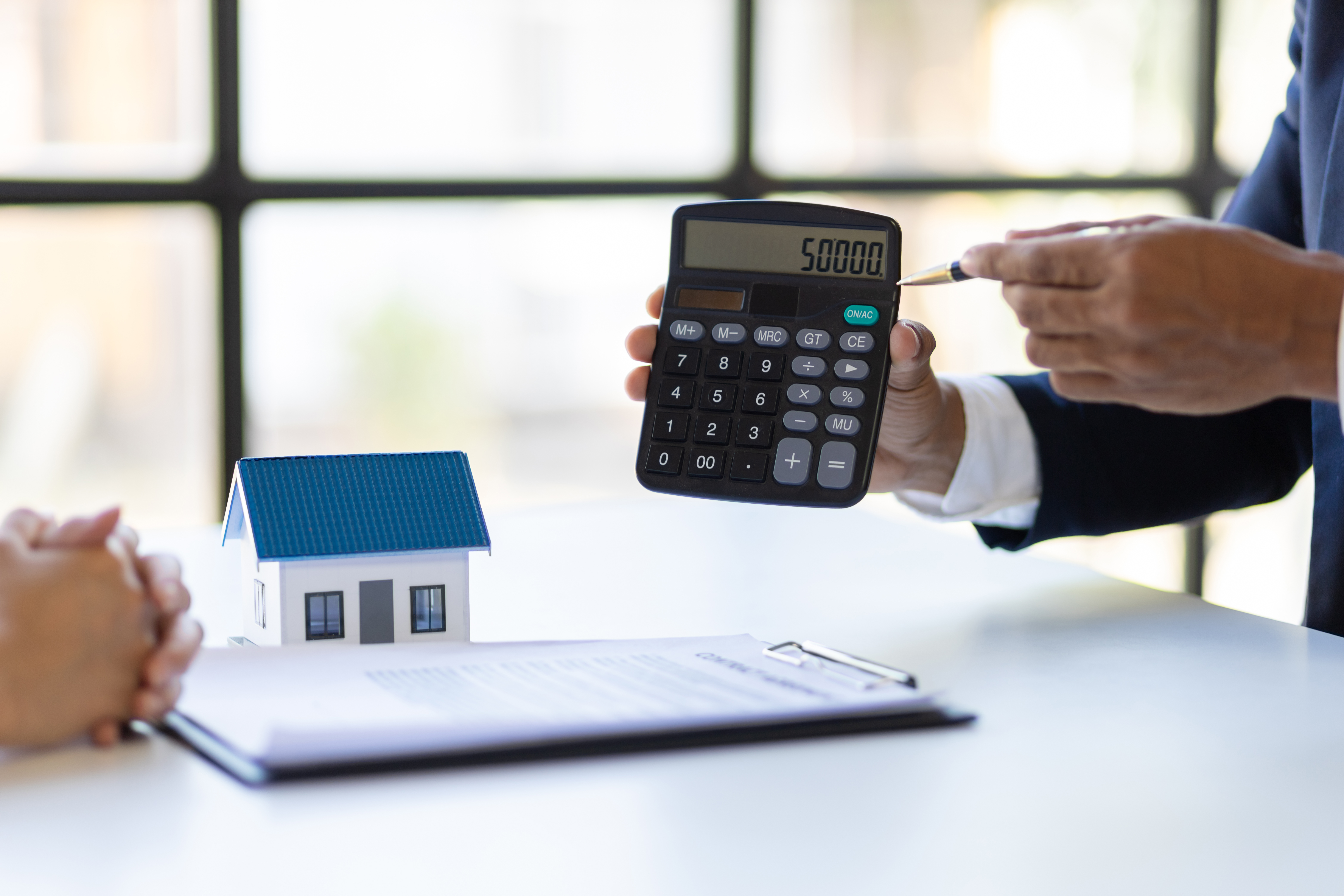 person-holding-calculator-showing-amount-next-to-miniature-house-model